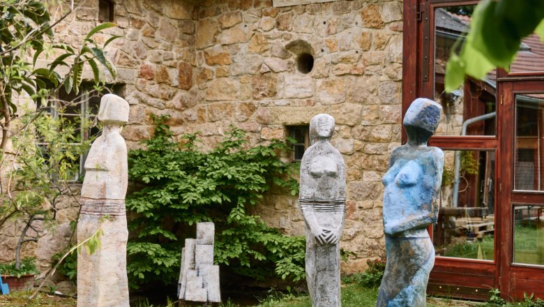 Three colorful sculptures stand on a meadow in front of an old stone building
