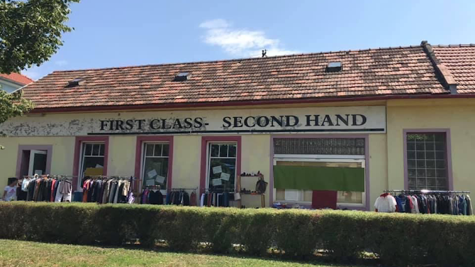 Second-Hand-Laden mit dem Namen 'First Class - Second Hand' auf einem gelben Gebäude mit rotem Ziegeldach.
