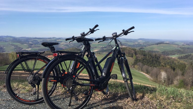 Zwei E-Bikes stehen auf einem Hügel mit Blick auf eine hügelige Landschaft.