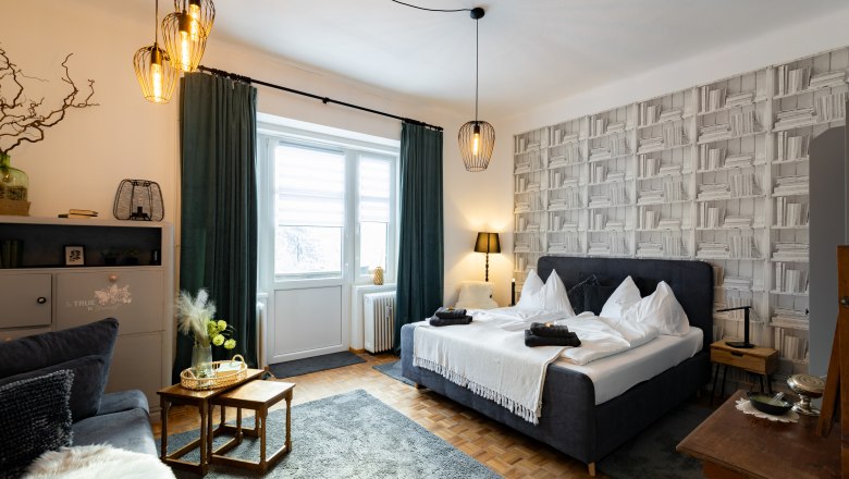 Gemütliches Schlafzimmer mit Doppelbett, dekorativen Lampen und Bücherregal-Tapete.