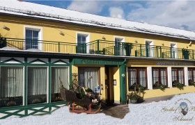 Yellow building with green accents, labeled Gasthof Schmirl, in the snow.