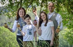 Eine Familie mit zwei Kindern steht auf einer Wiese und hält verschiedene Honigprodukte.