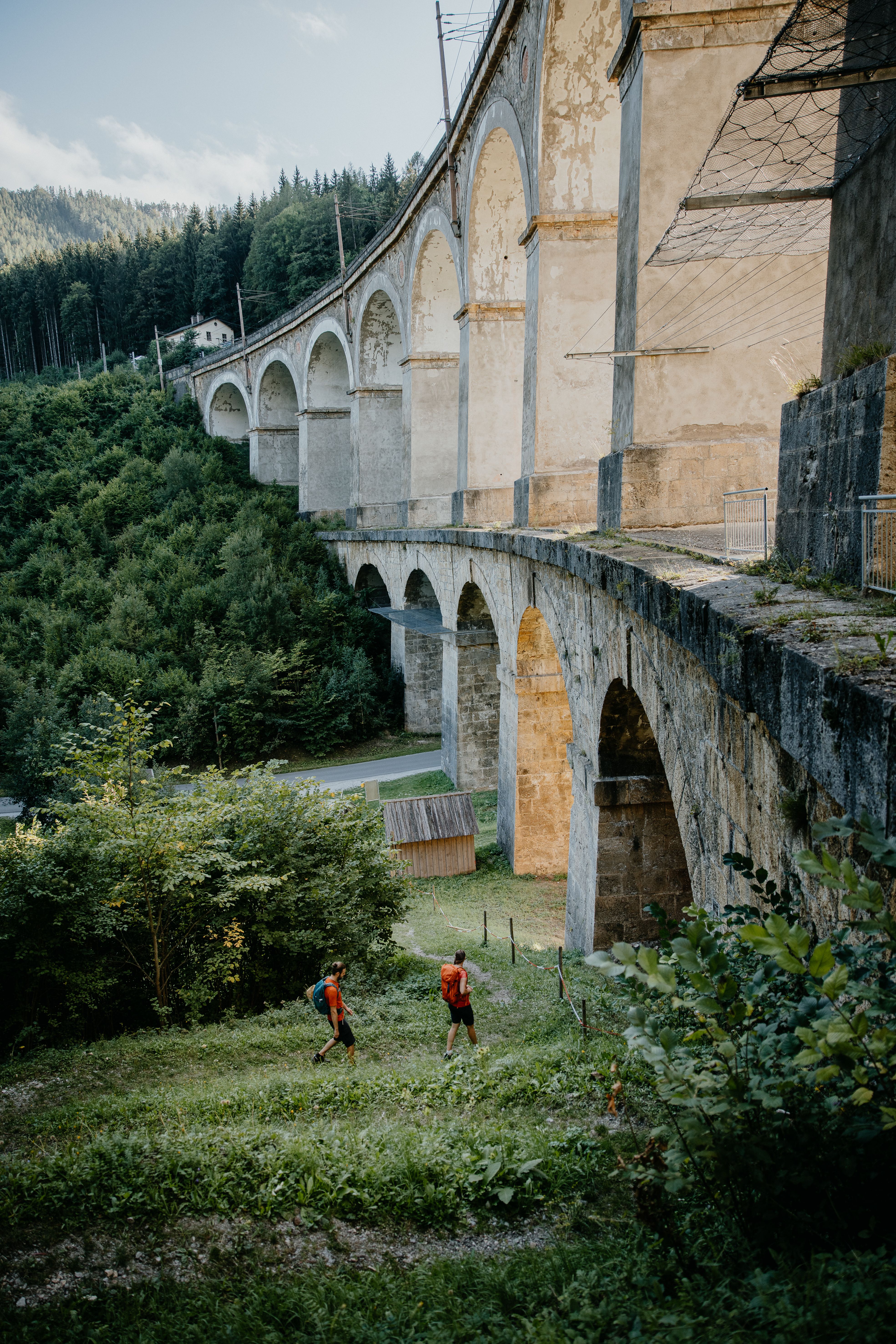 Ein Wanderer blickt auf einen Zug, der gerade über ein Viadukt fährt.