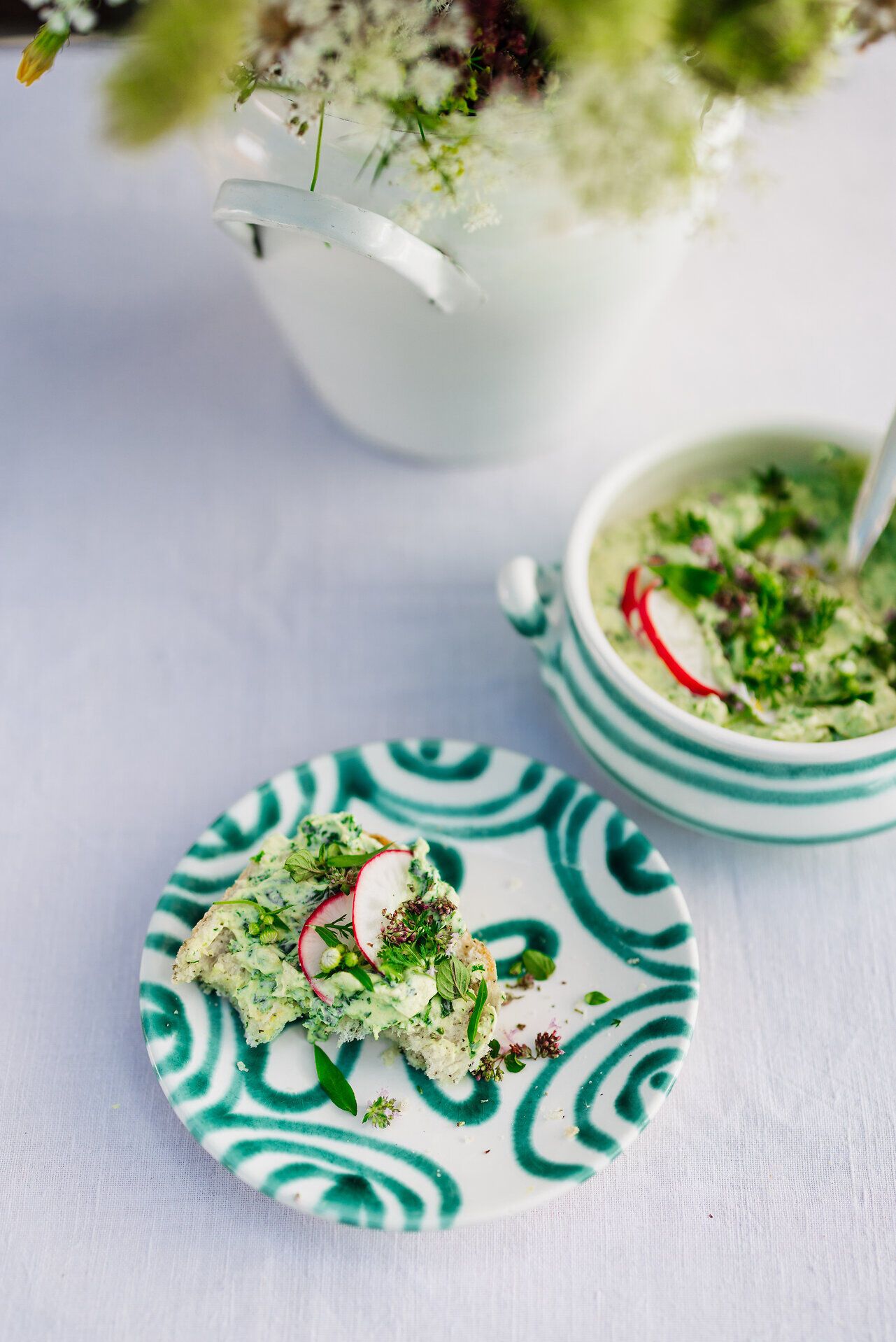 Ein köstlicher Wildkräuteraufstrich auf einem kunstvoll dekorierten Teller lädt dazu ein, die Aromen der Natur zu entdecken. Frische Radieschen und grüne Kräuter verleihen dem Gericht eine lebendige Note, während die sanfte Atmosphäre des Berggasthofs zum Verweilen einlädt.