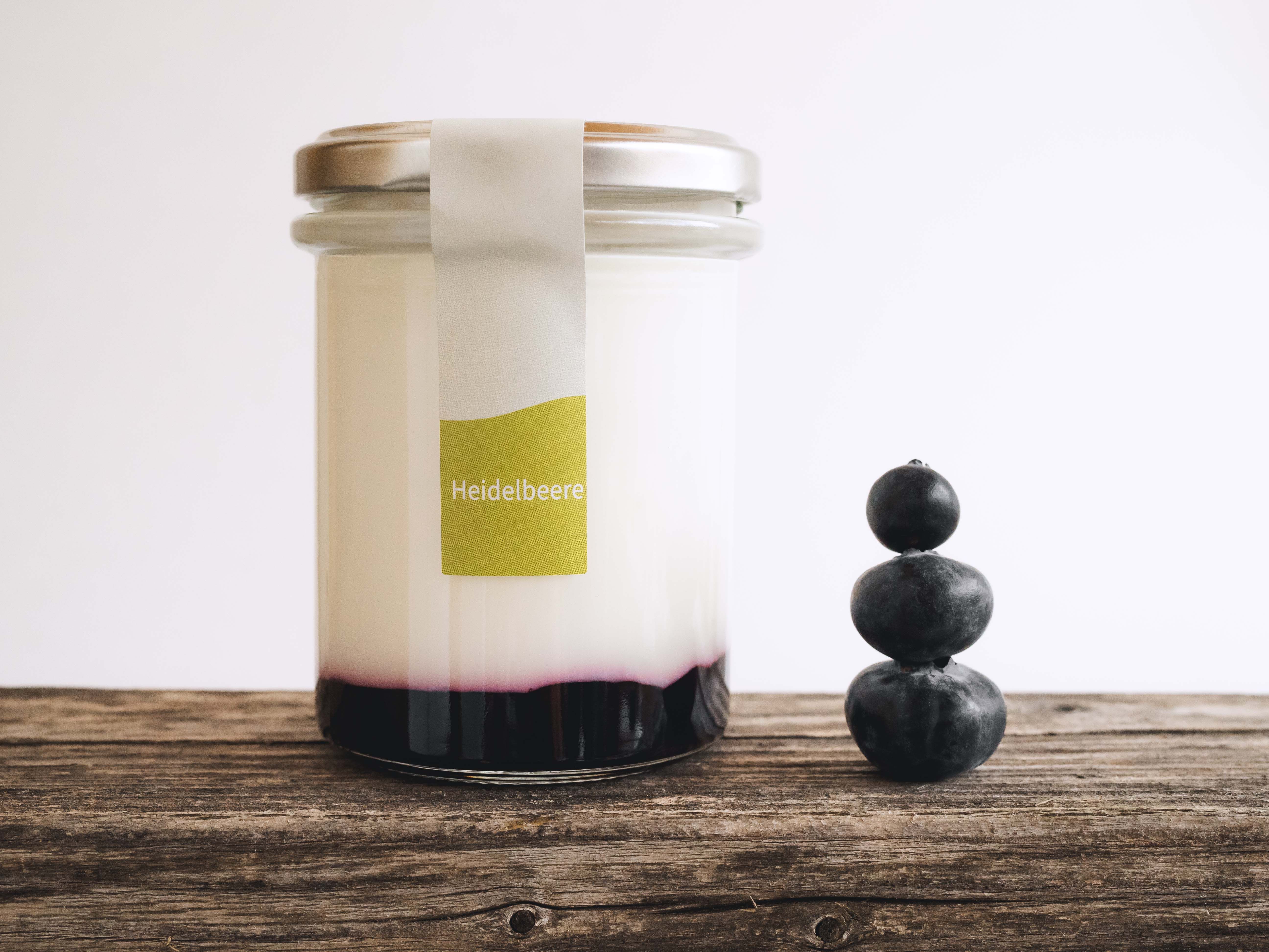 las mit Naturjoghurt und Heidelbeerspiegel, daneben gestapelte Beeren auf Holzboden