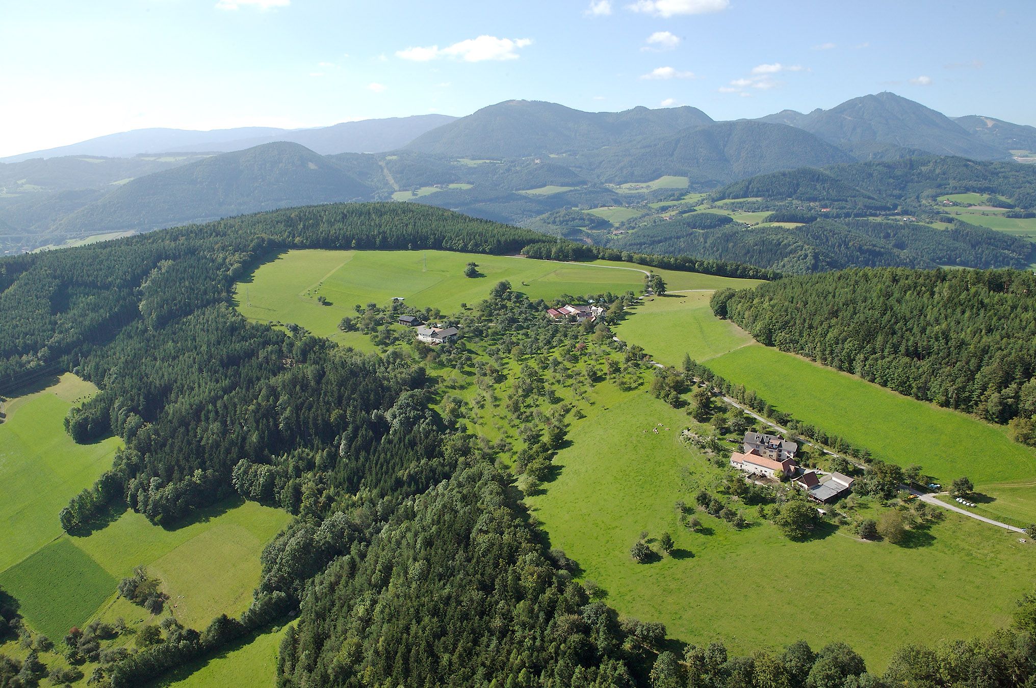 Luftaufnahme von Prigglitz mit grünen Wiesen und Wäldern, umgeben von Bergen.