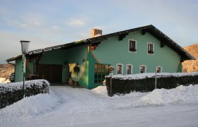 Grünes Haus im Schnee mit dekorativen Elementen und Laterne.