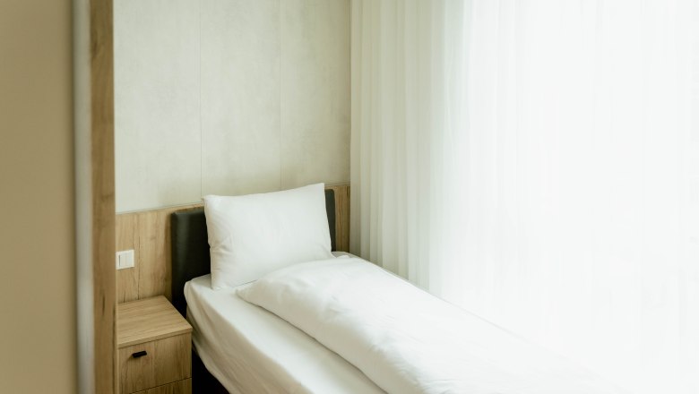 Einzelbett in einem hellen Hotelzimmer mit weißer Bettwäsche und einem Nachttisch.