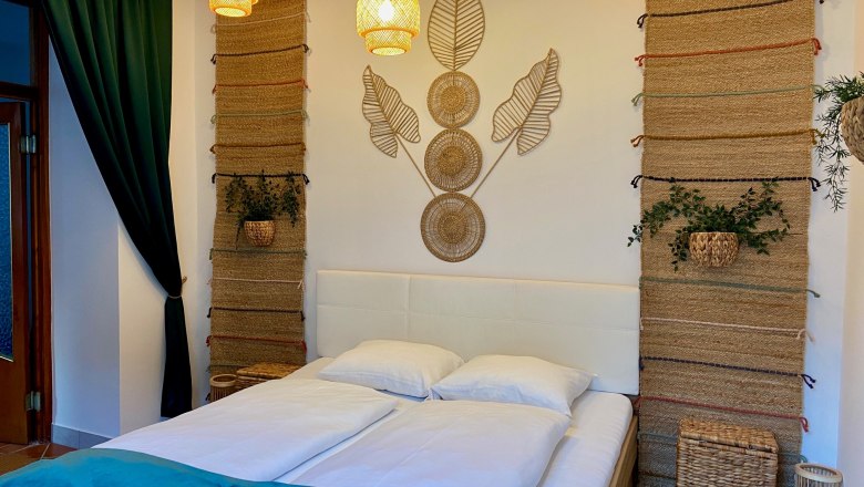 Zemlinsky Hof, © Wiener Alpen Ein gemütliches Schlafzimmer mit einem Doppelbett, dekorativen Wandteppichen und Pflanzen.