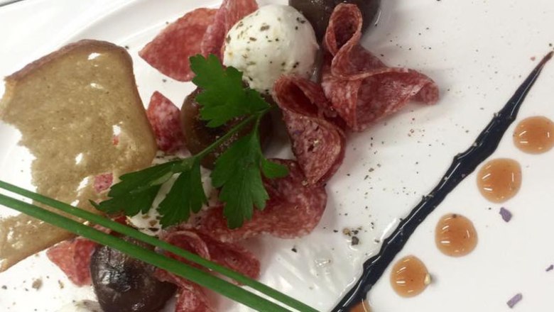 A plate with salami, a goat's cheese ball, herbs and a piece of bread.