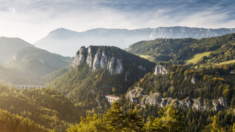 Panoramablick auf eine Berglandschaft mit Viadukt und bewaldeten Hügeln.