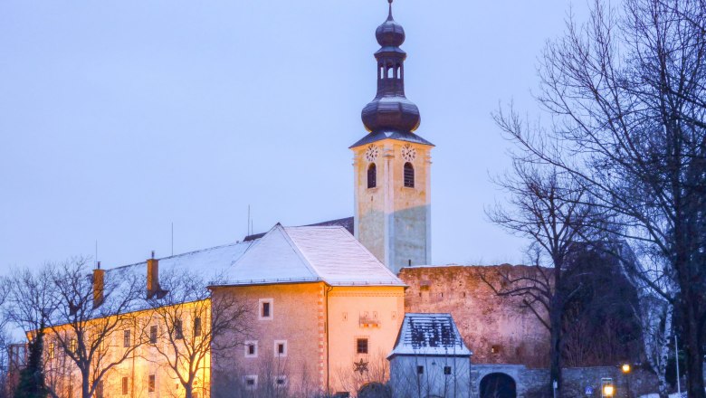 Gloggnitz Castle in winter with illuminated tower and snow-covered roof.