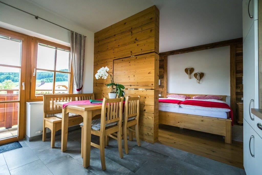 Gemütliches Zimmer mit Holzmöbeln, Esstisch, Stühlen und einem Bett. Fenster mit Blick auf grüne Landschaft.