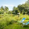 Two blue deckchairs on a meadow on the banks of a pond, surrounded by green vegetation.