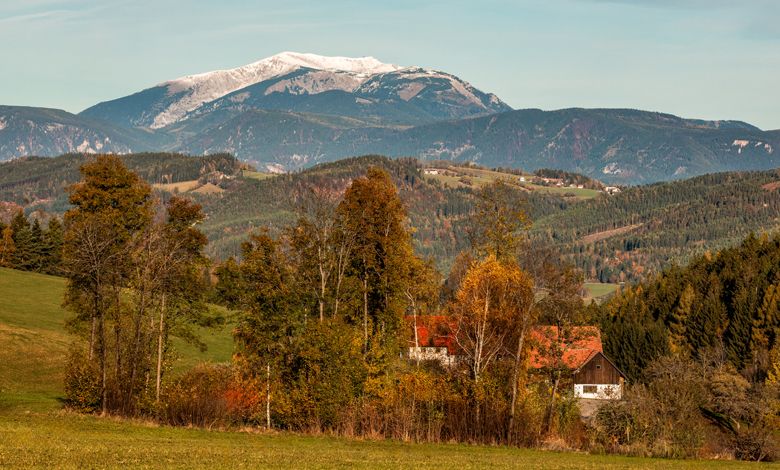 Landschaft mit Bergen, Bäumen und einem Haus im Herbst.