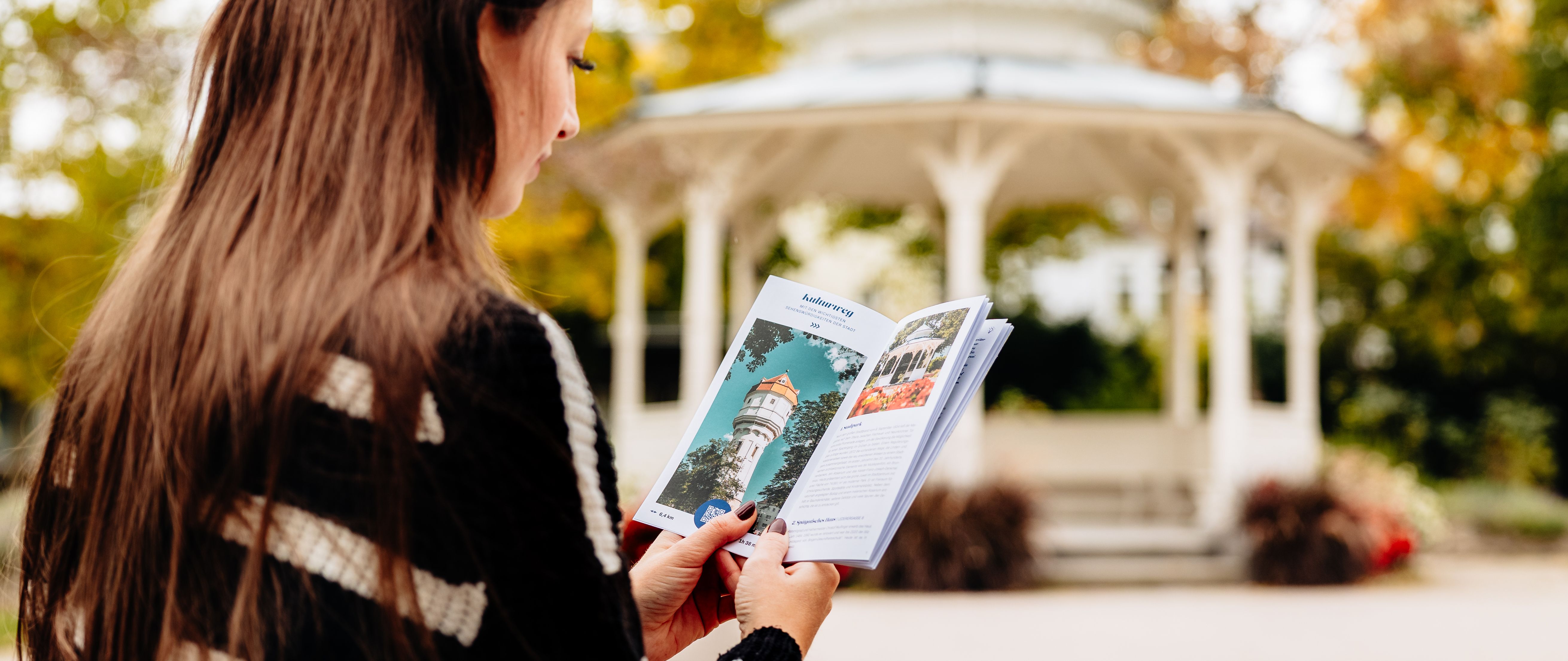 Frau liest einen Flyer vor einem Pavillon. 