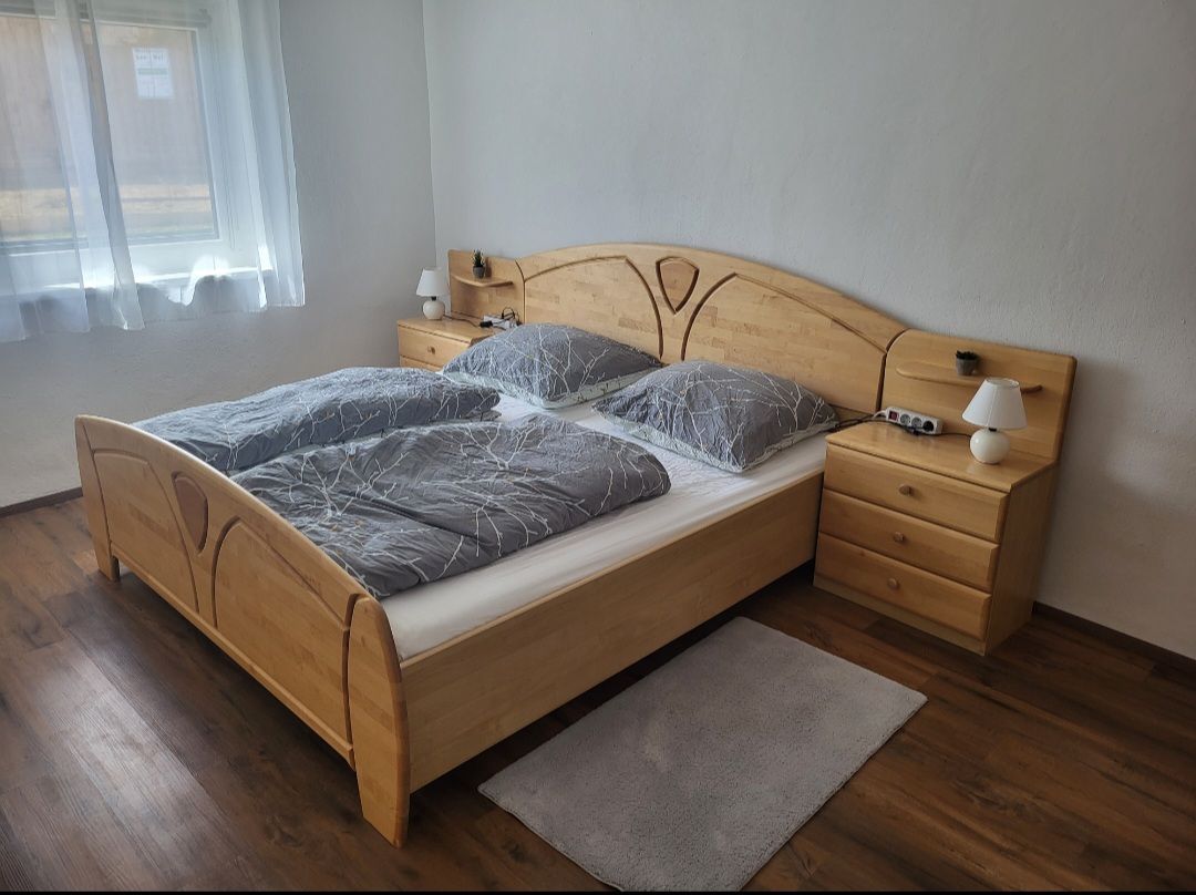 Schlafzimmer mit Doppelbett, Holzmöbeln und grauer Bettwäsche.