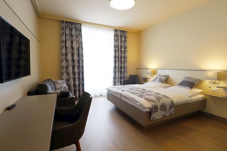 Modern eingerichtetes Hotelzimmer mit Doppelbett, Schreibtisch, Fernseher und Sesseln.