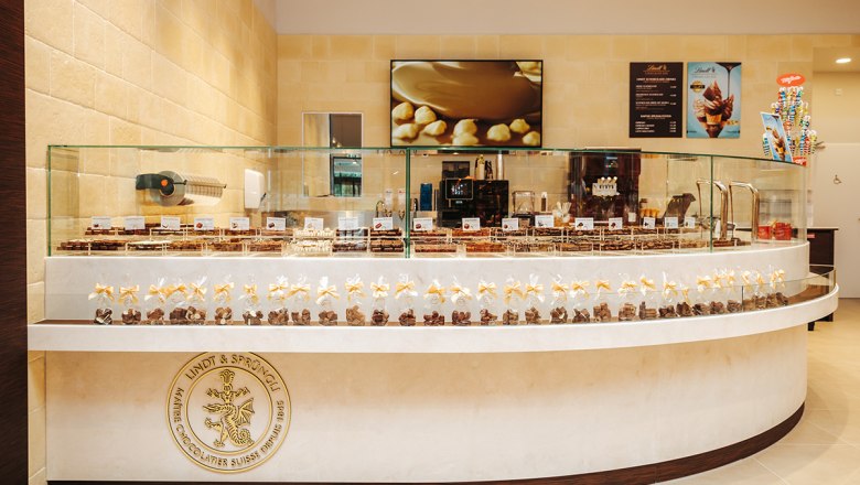 Innenansicht eines Schokoladengeschäfts mit Pralinen in Glasvitrinen und einem Lindt & Sprüngli Logo.