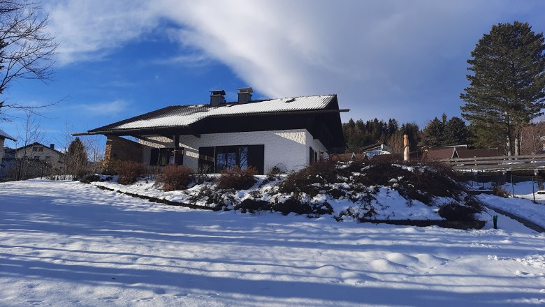 A snow-covered house in winter with a blue sky and trees in the background.
