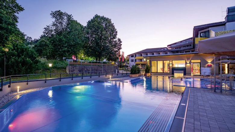 Beleuchtete Poolanlage bei Nacht mit Gebäuden im Hintergrund.