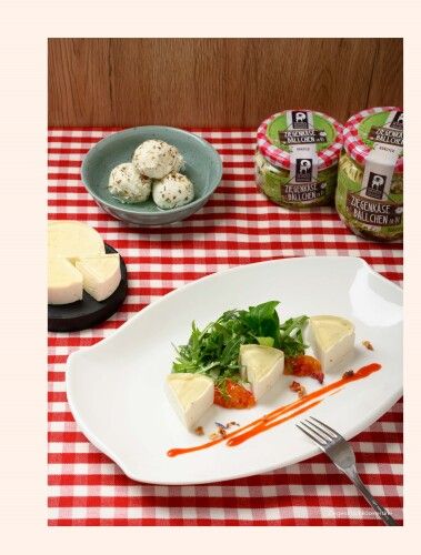 Teller mit Ziegenfrischkäseterrine auf kariertem Tischtuch, daneben Ziegenkäsebällchen.