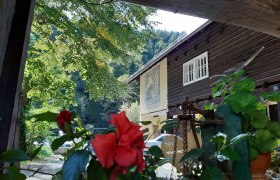 Ein traditionelles Holzhaus mit roten Blumen im Vordergrund und grünen Bäumen im Hintergrund.