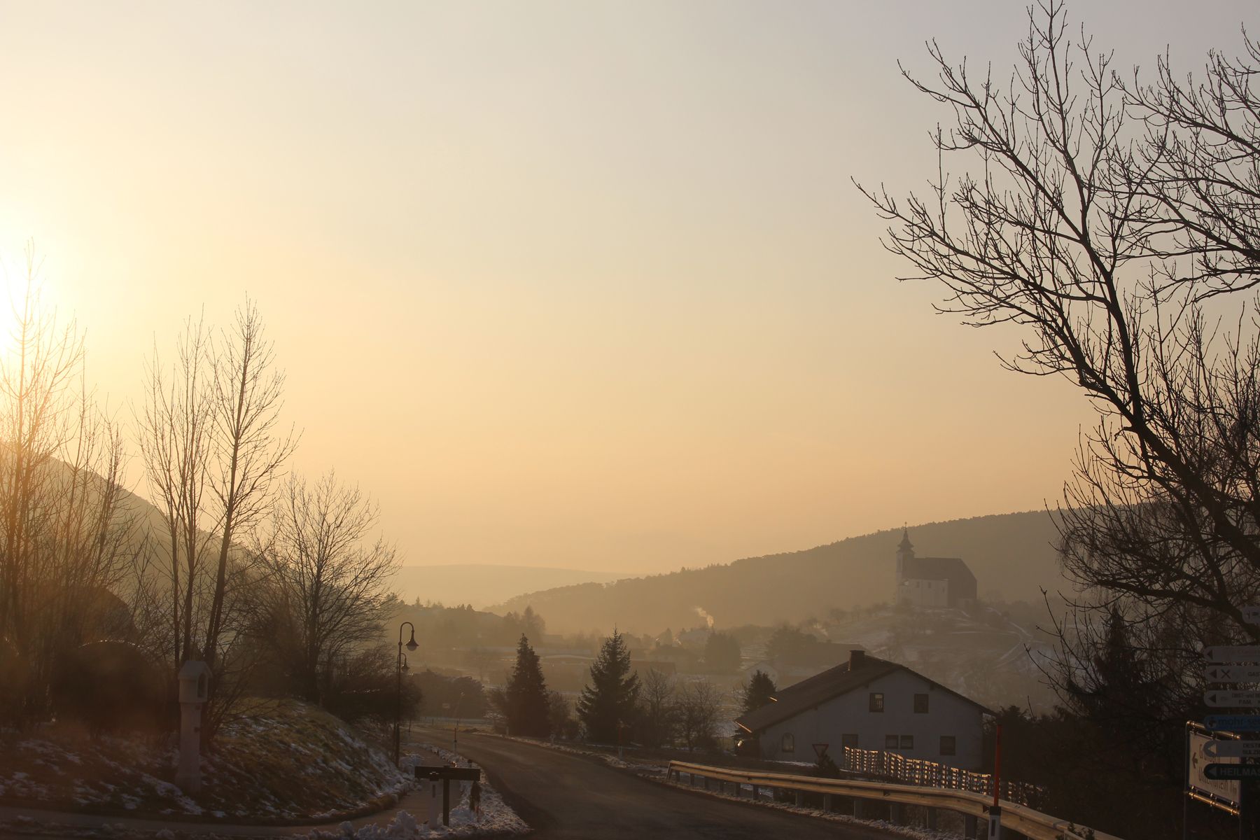 Landschaft bei Sonnenaufgang mit Kirche im Hintergrund.