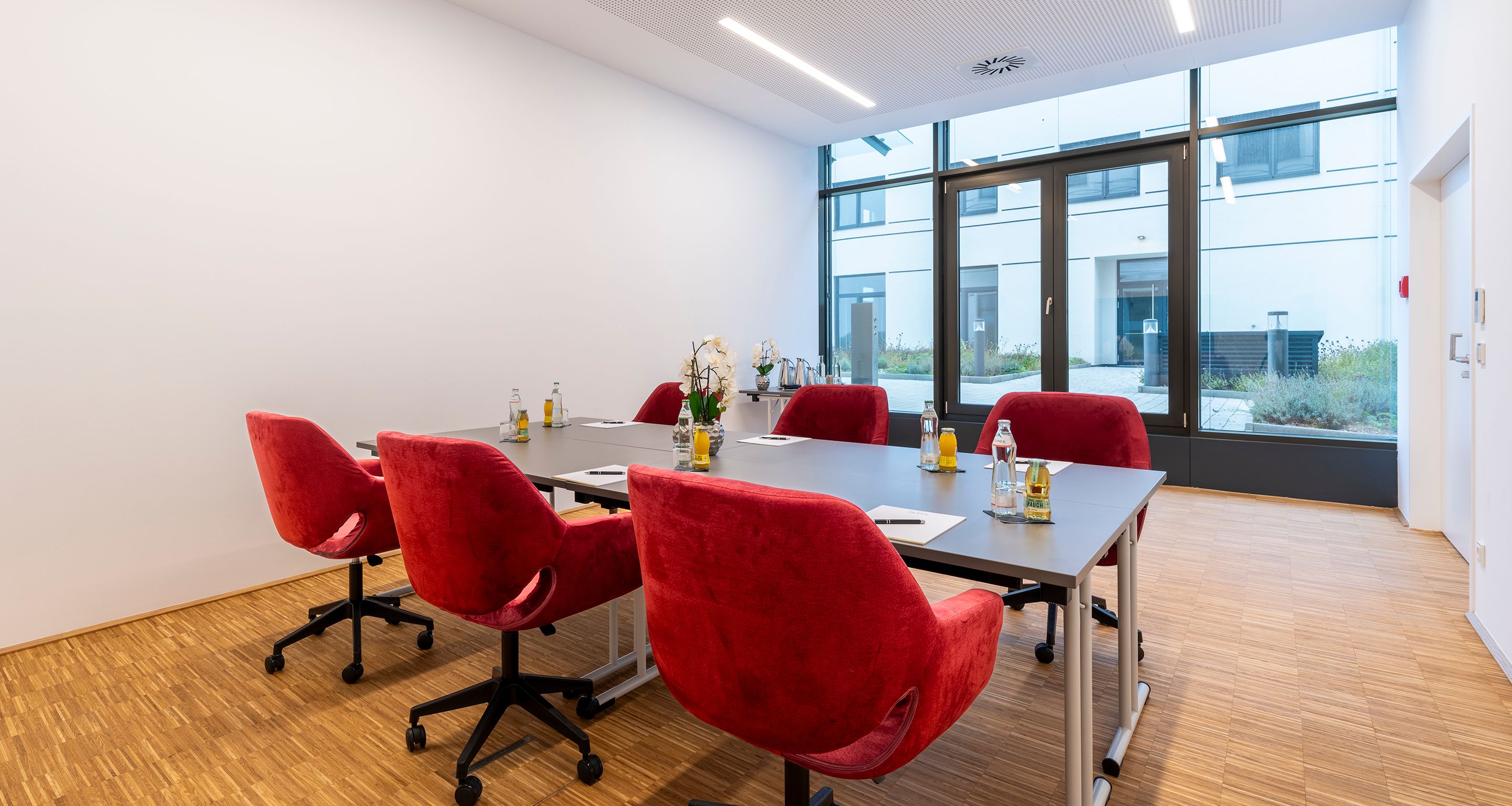 Kleiner Seminarraum mit Terrasse und großen Fenstern, roten, bequemen Samtstühlen und Tisch für 6-8 Personen