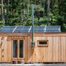 Kleines Holzhaus mit Solarpanelen auf dem Dach im Wald.