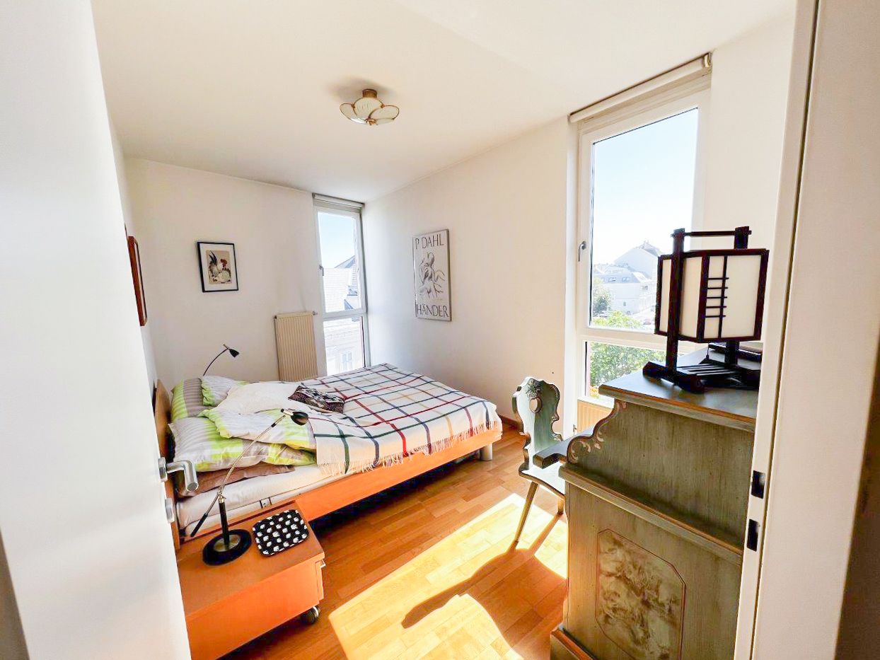 Helles Schlafzimmer mit Bett, Schreibtisch und Fenster.