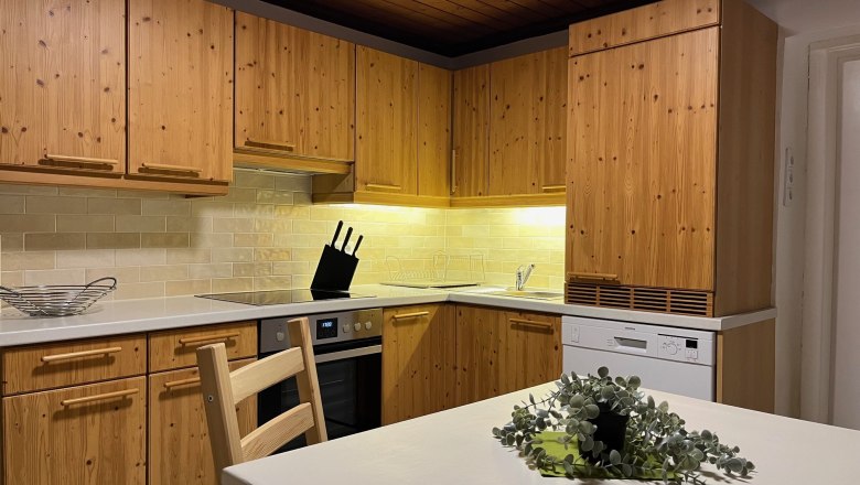 Küche mit Holzmöbeln, Herd, Spülmaschine und Tisch mit Pflanze.