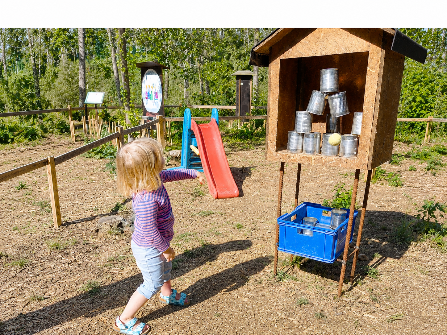 Ein Kind wirft einen Ball auf gestapelte Dosen in einem Freiluftspielplatz.