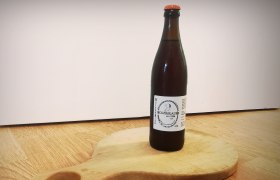 Eine Flasche Weizenbier vom Holzbräu steht auf einem runden Holzbrett mit Griff.