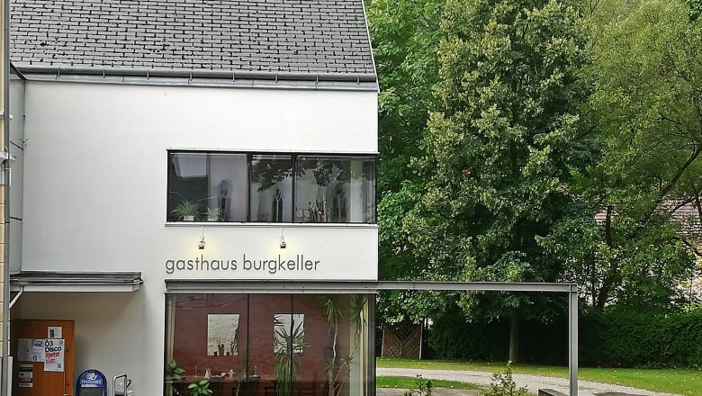 Modern building with the inscription 'Gasthaus Burgkeller', surrounded by trees.