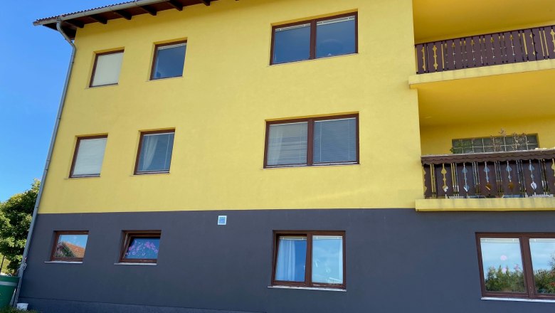 Gelbes Gebäude mit braunen Fenstern und Balkonen, blauer Himmel im Hintergrund.