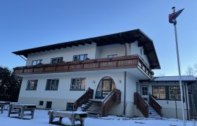 Ein zweistöckiges Gebäude mit Holzbalkon und Treppen, umgeben von Schnee, unter klarem Himmel.