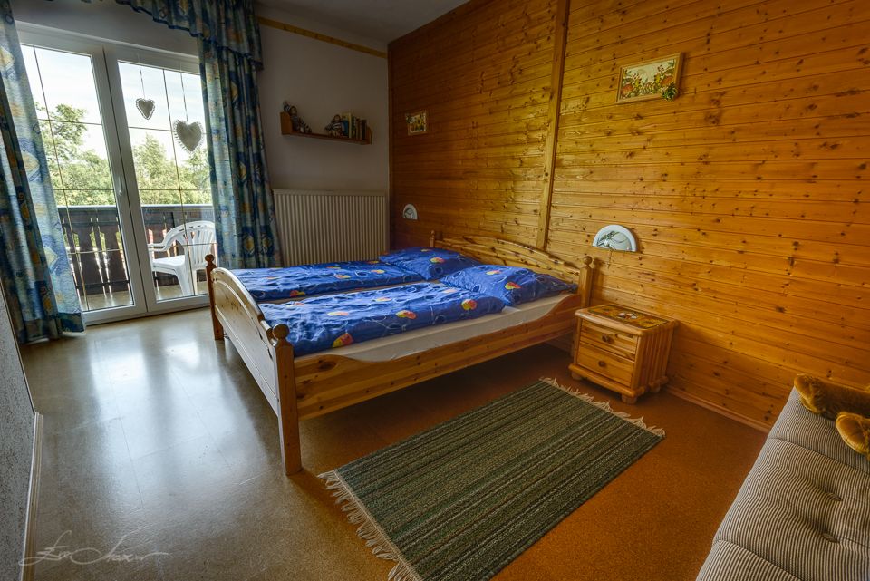 Gemütliches Schlafzimmer mit Holzwänden, Doppelbett, blauem Bettzeug und Balkon mit Blick ins Grüne.