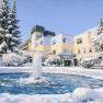 Ein Gesundheitsresort im Winter mit schneebedeckten B&auml;umen und einem gefrorenen Brunnen im Vordergrund.