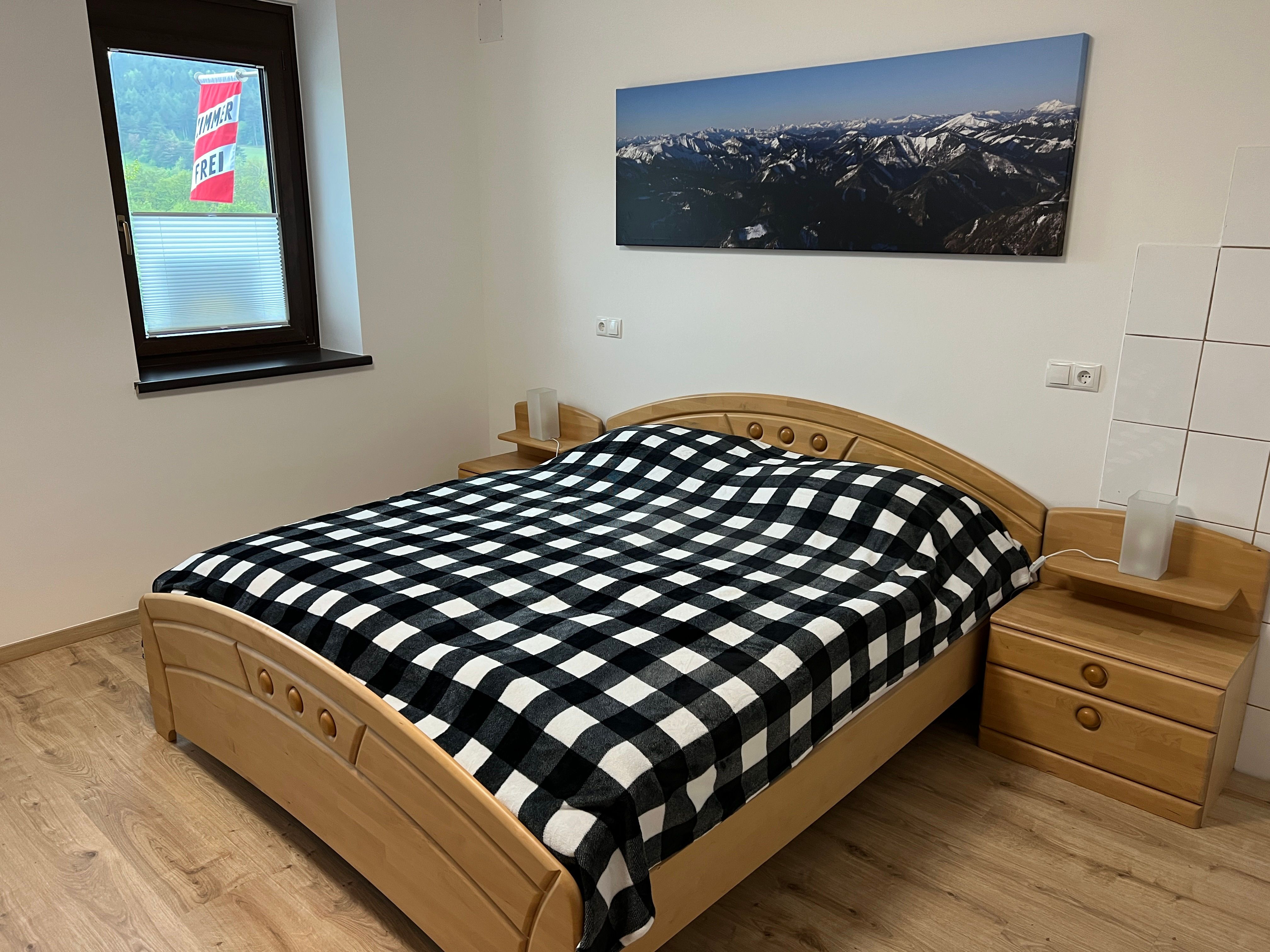 Schlafzimmer mit Doppelbett, kariertem Bettbezug und Bergbild an der Wand.