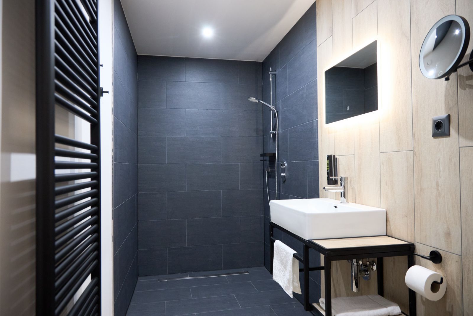 Barrier-free, large shower in the bathroom with washbasin, WC, mirror and towel warmer.