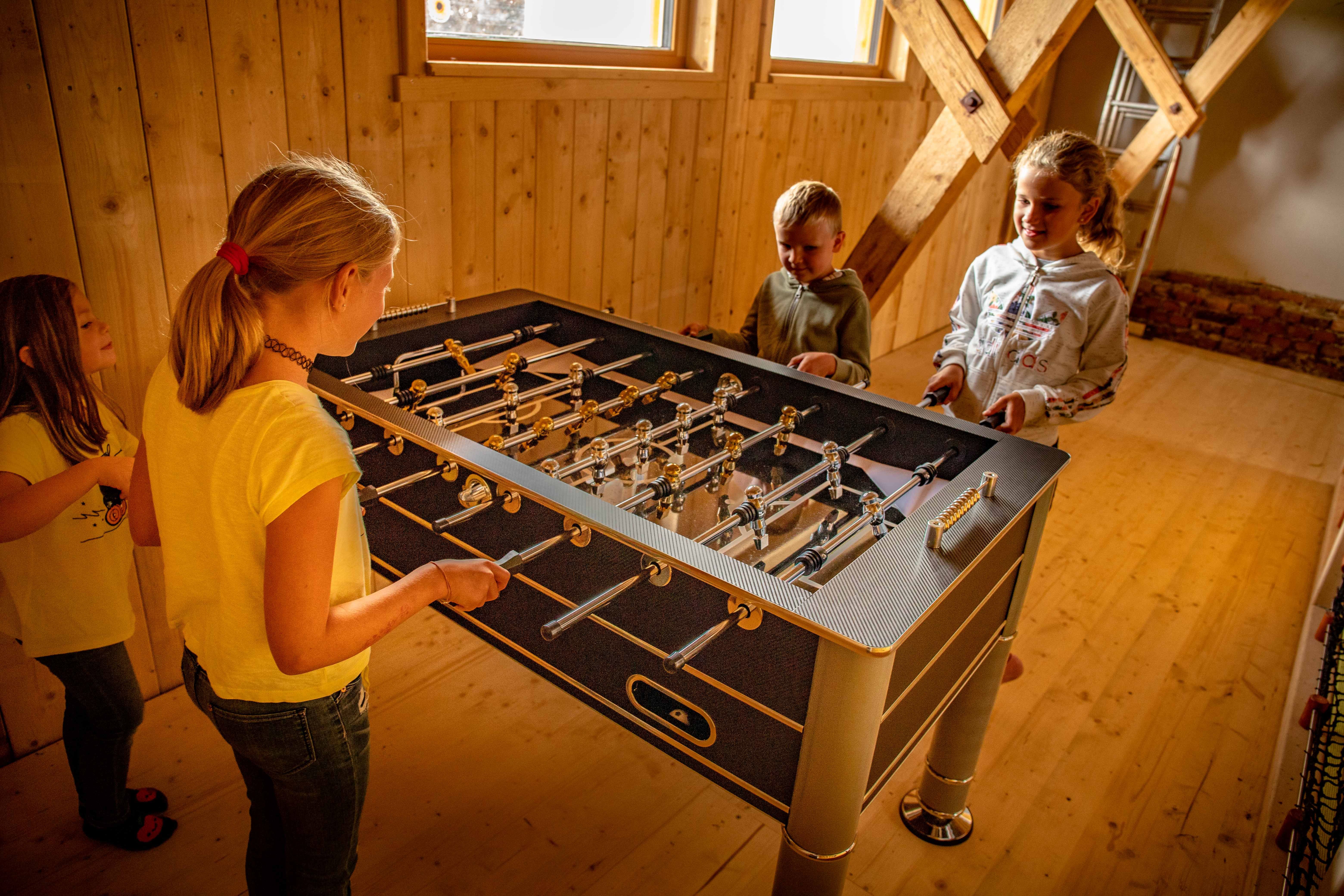 Kinder spielen Tischfußball in einem Holzraum.