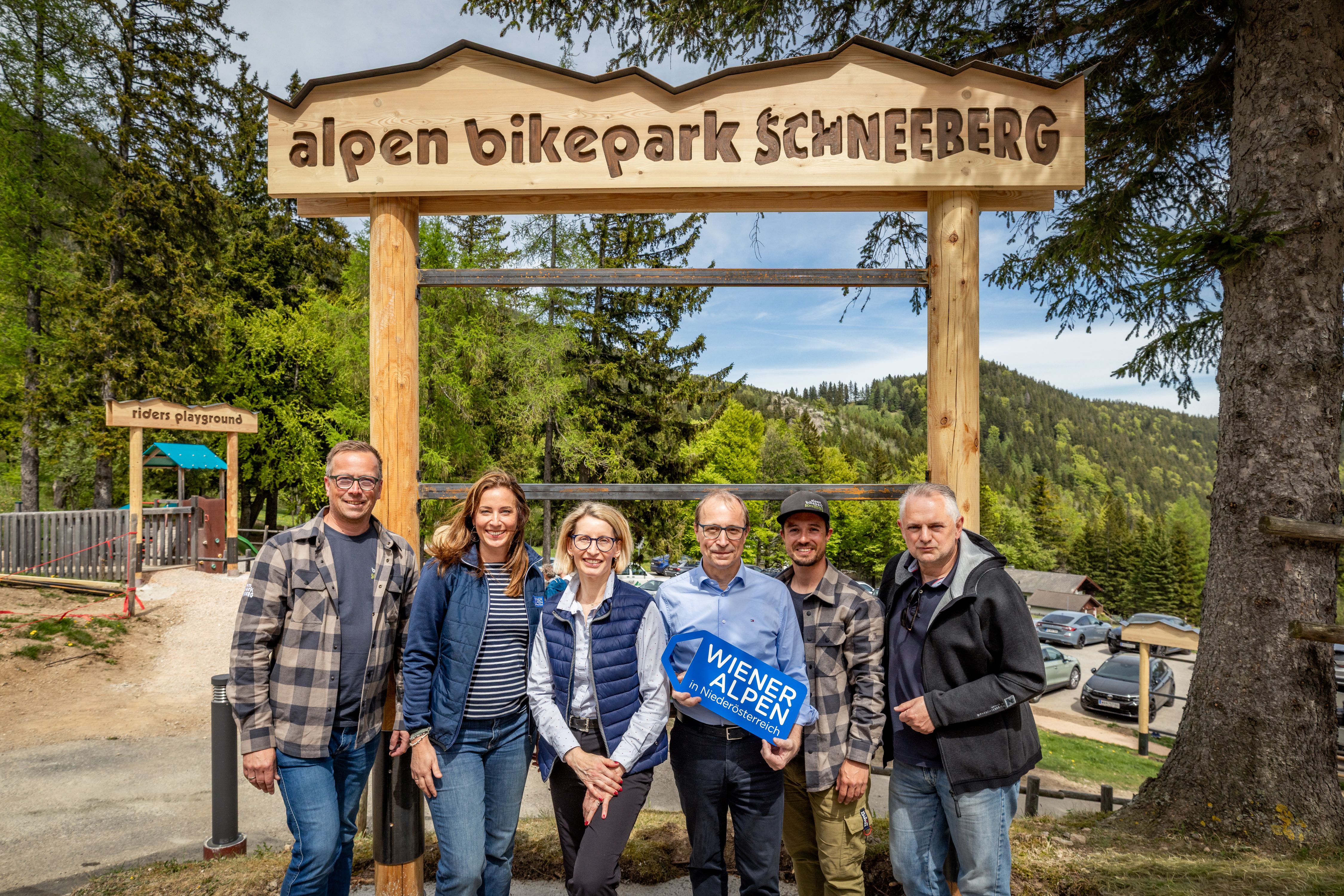 Sechs Personen stehen vor einem alpen bikepark Schneeberg Schild. Eine Person hält ein Wiener Alpen-Logo Schild in den Händen.
