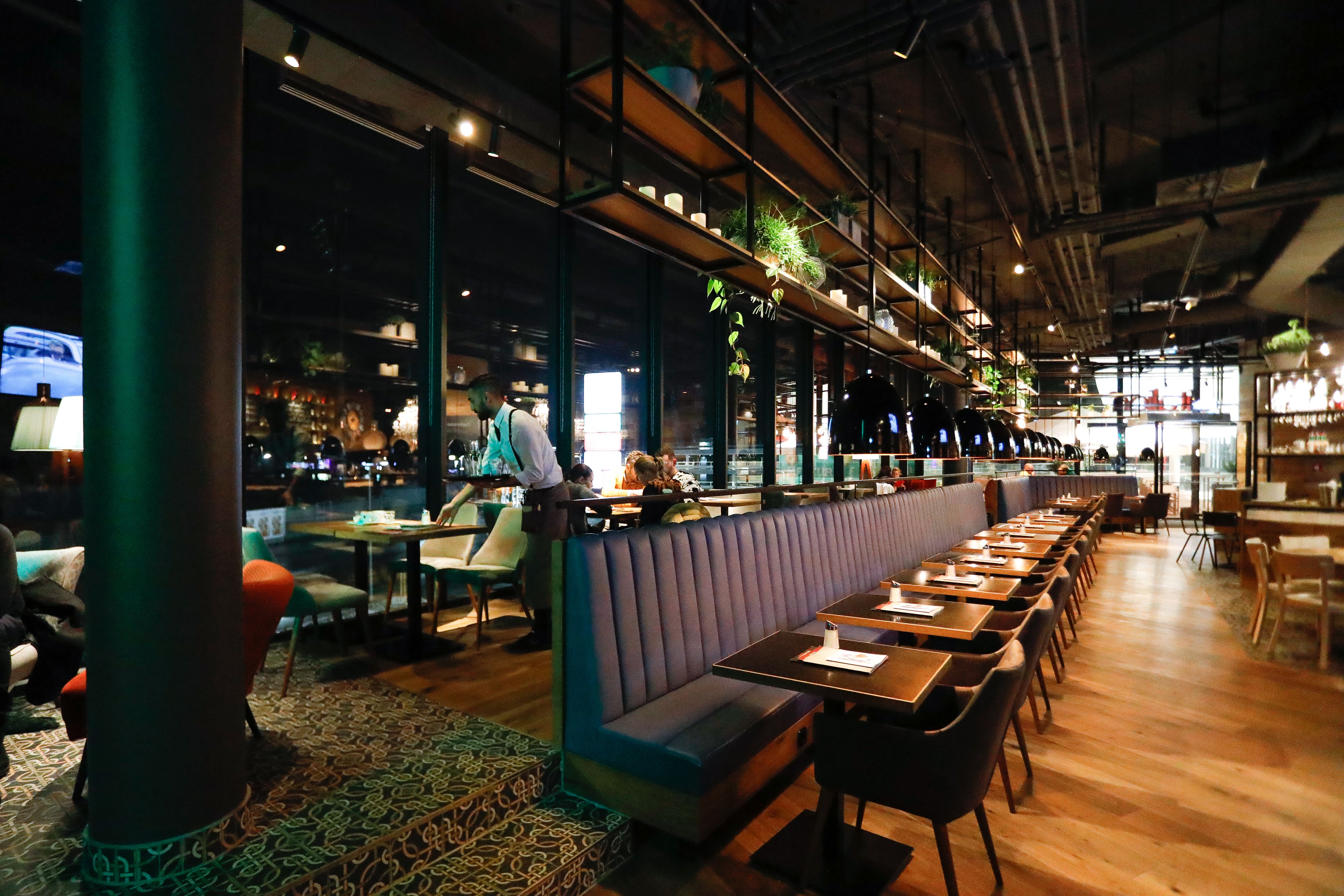 Innenansicht eines modernen Restaurants mit langen Tischen und Pflanzen.