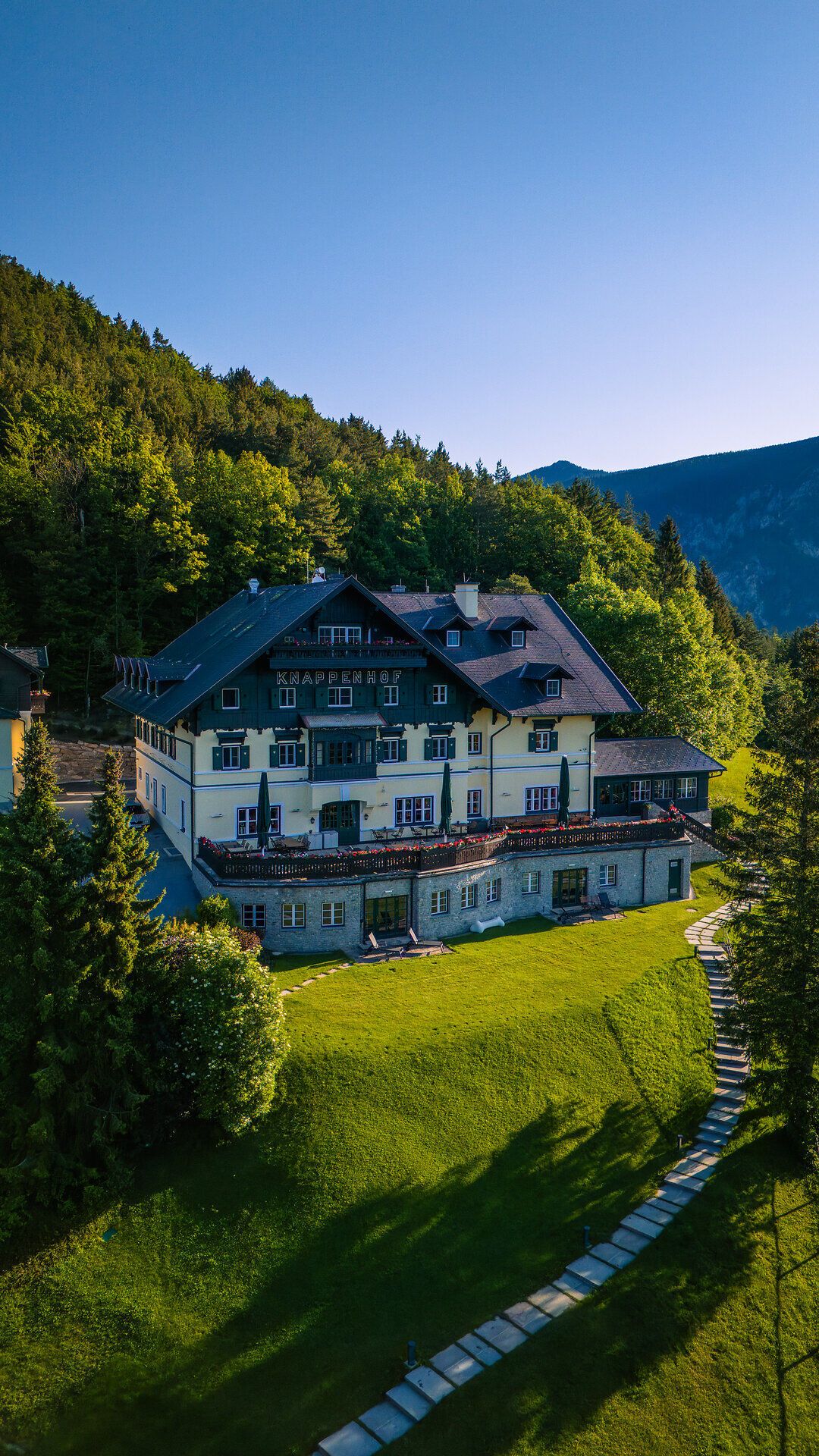 Umgeben von üppigem Grün und majestätischen Bergen, strahlt der Knappenhof eine einladende Ruhe aus. Die harmonische Architektur des Hauses fügt sich perfekt in die malerische Landschaft ein und lädt dazu ein, die Schönheit des Bergsommers in den Wiener Alpen zu genießen.