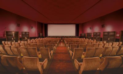 Leerer Kinosaal mit roten Wänden und beigen Sitzen und Leinwand