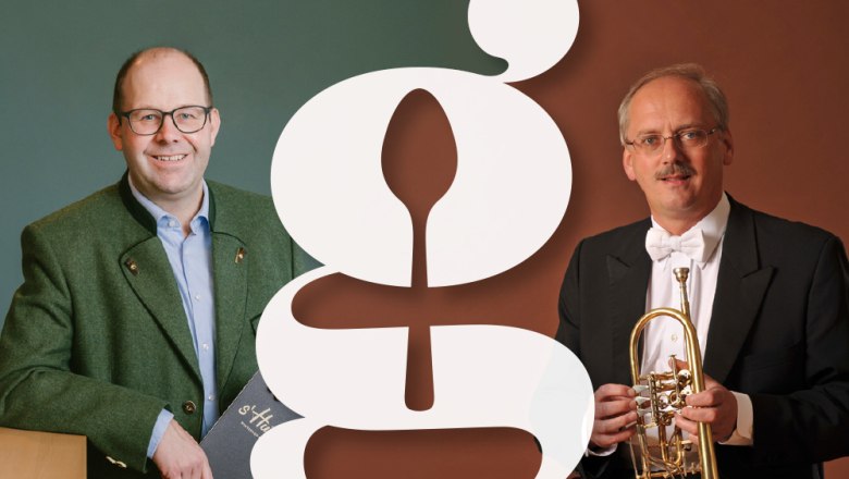 Zwei M&auml;nner in Anz&uuml;gen mit einem gro&szlig;en stilisierten Buchstaben im Vordergrund.