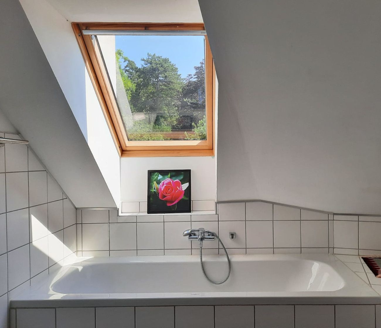 Badezimmer mit Dachfenster und Badewanne, darunter ein Bild einer roten Rose.