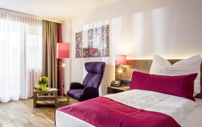 Gemütliches Zimmer mit Doppelbett, Ohrensessel, Tisch, Lampen, einem Wandbild und Holzboden.