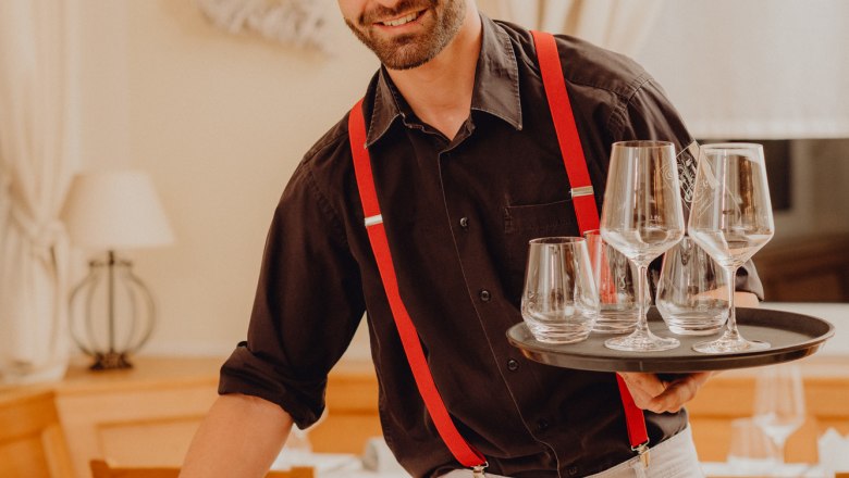 Č&iacute;&scaron;n&iacute;k s červen&yacute;mi &scaron;lemi pod&aacute;v&aacute; v restauraci skleničky.